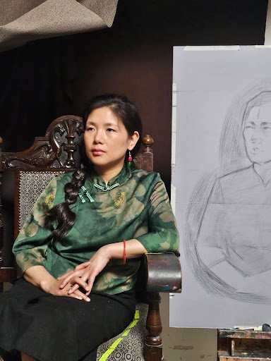 Jie posing in the studio, with a preliminary sketch visible on the easel behind her